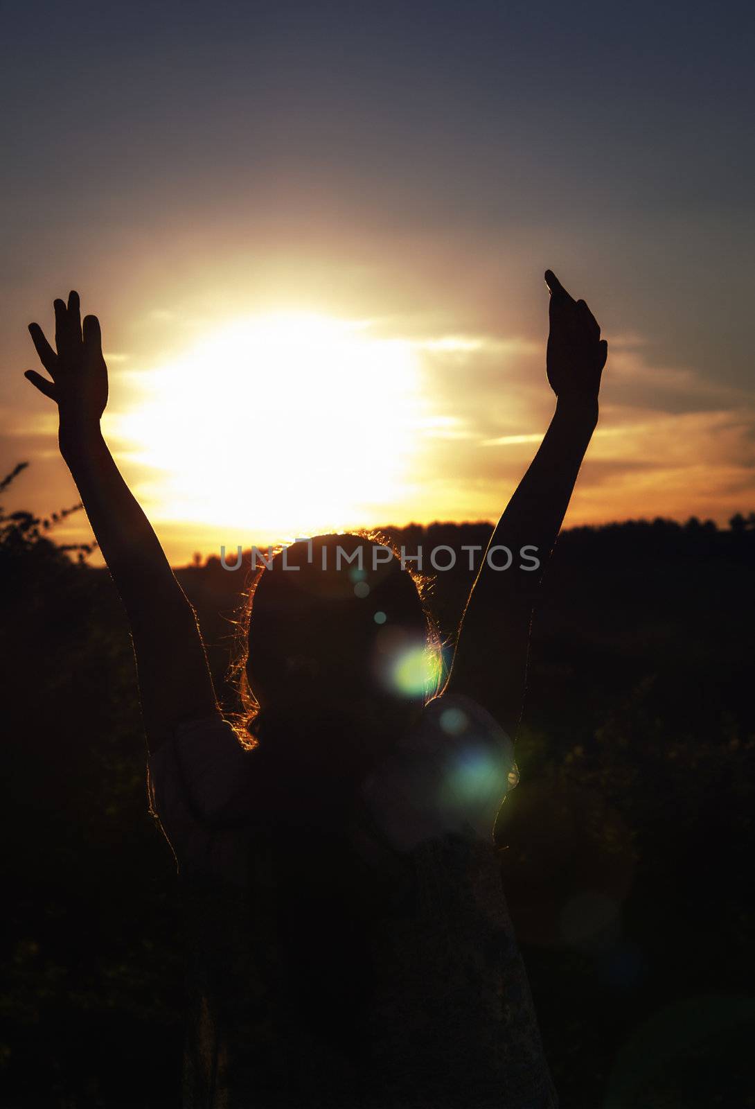 Young girl with hands up surrounding the sun at sunset