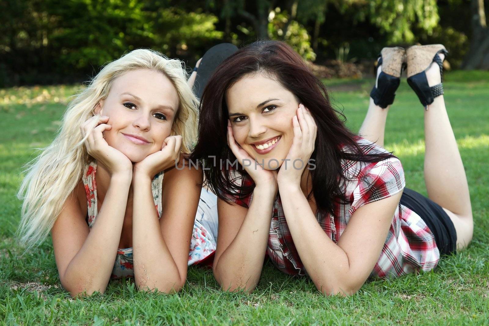 Two gorgeous smiling young women friends lying on the grass in a park