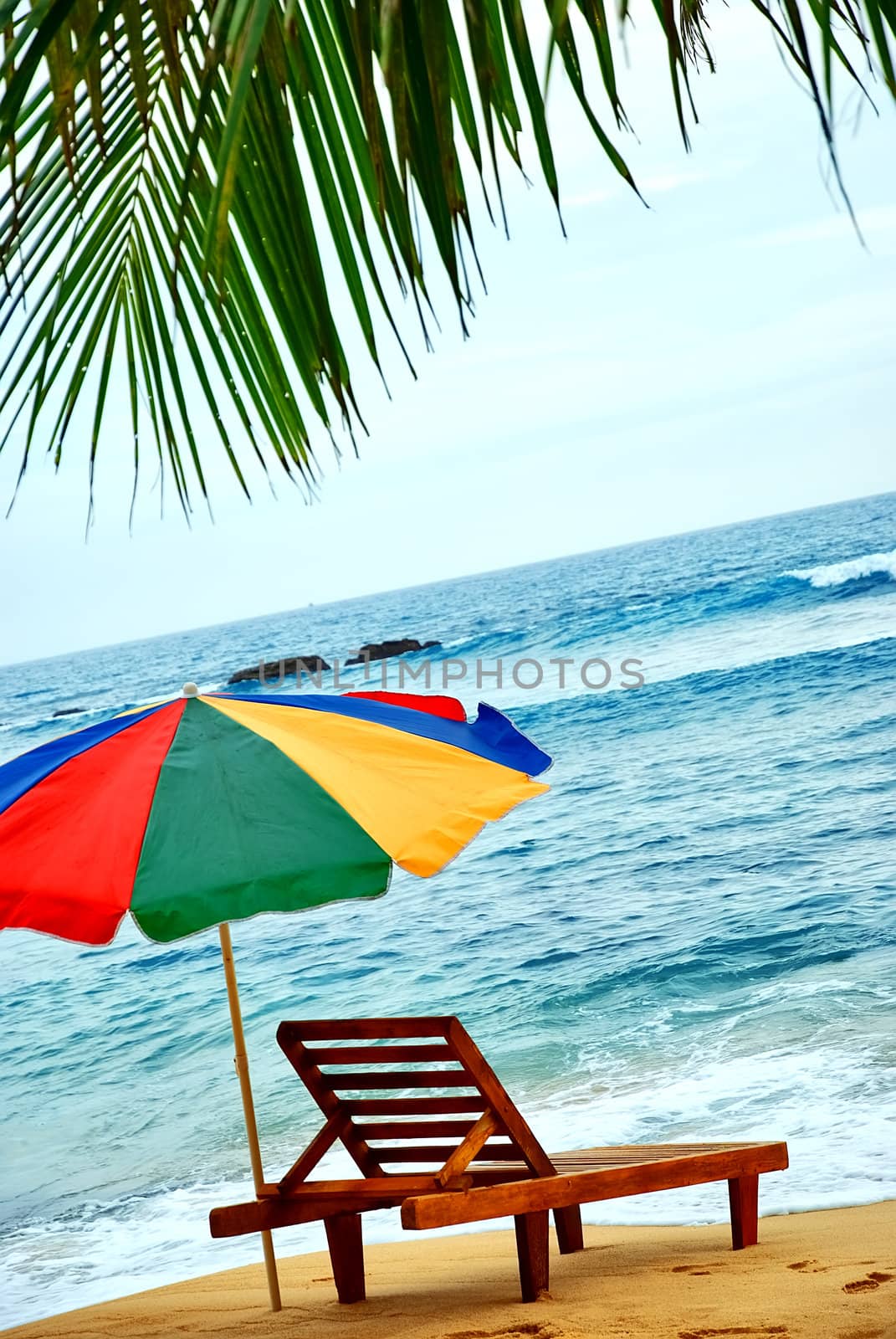 umbrella and lounge chair on the shore of exotic island with palm trees