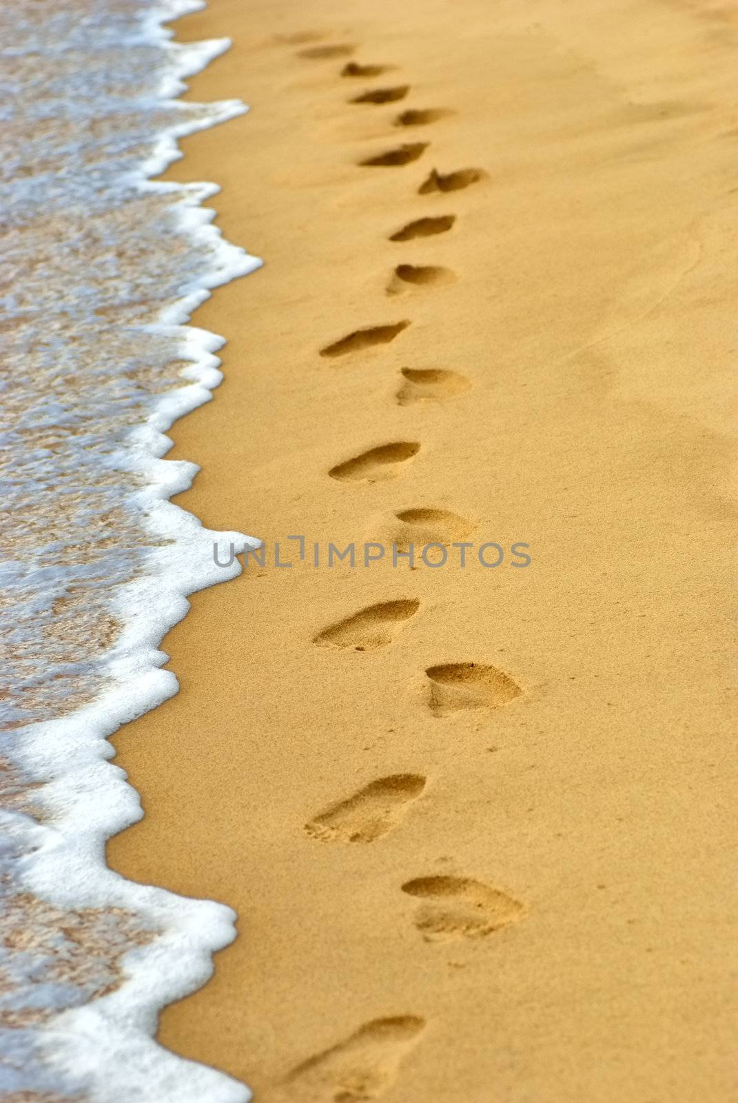 Ocean wave wash away human footprints on sand at the beach