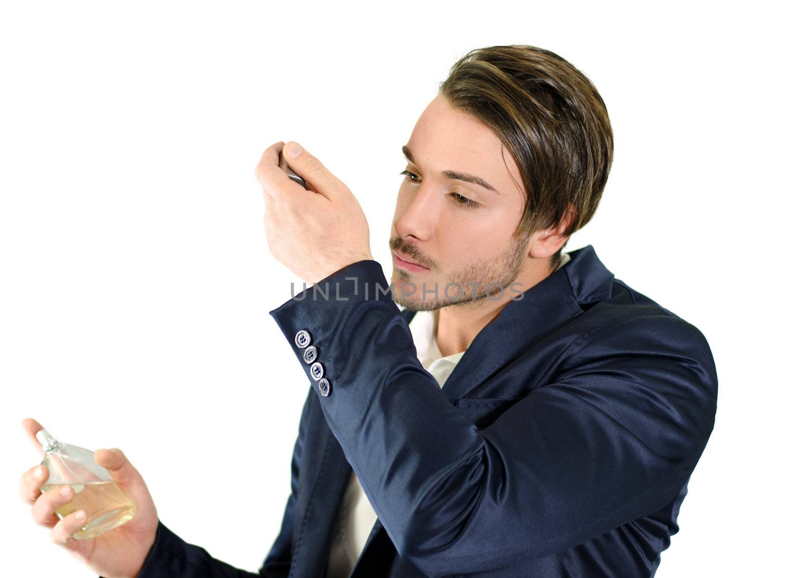 Attractive young man spraying and smelling fragrance or cologne, isolated