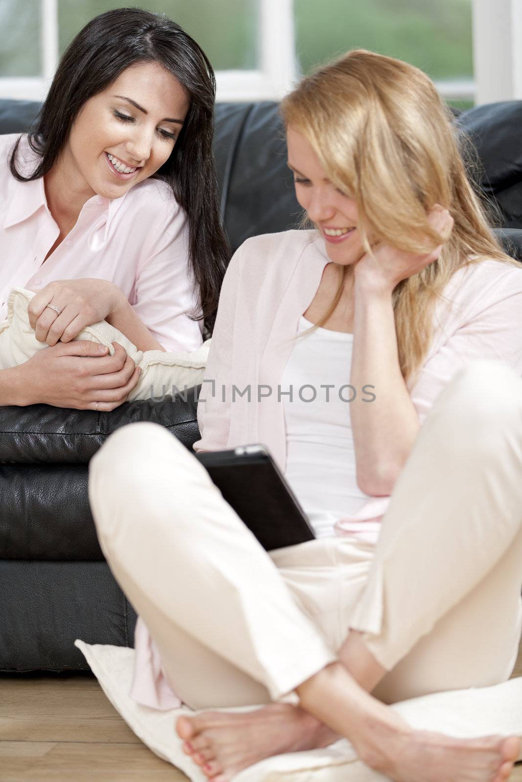 Two woman in their sitting room chatting and having fun on an electronic tablet