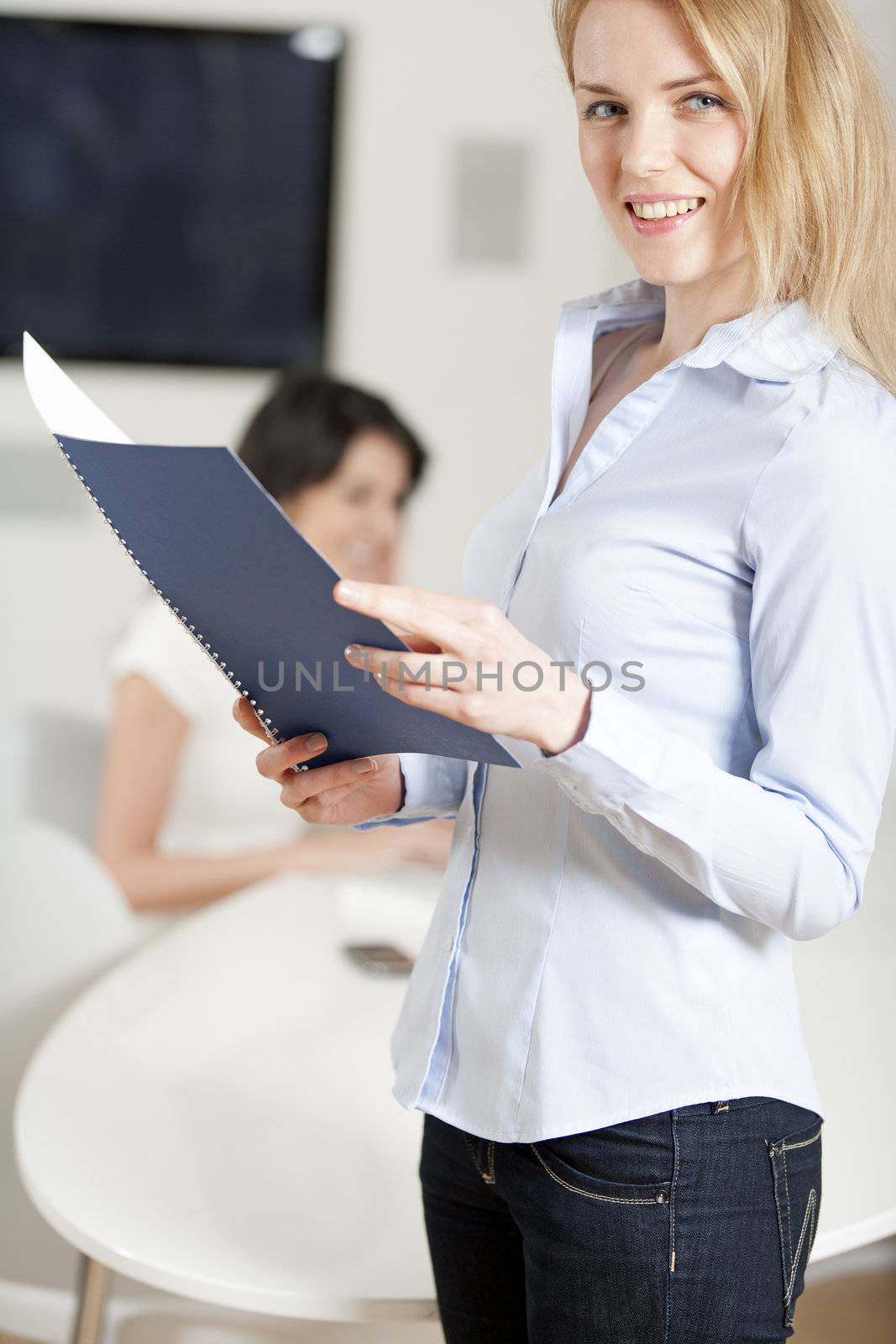 Two colleagues working in an office; one is in the background