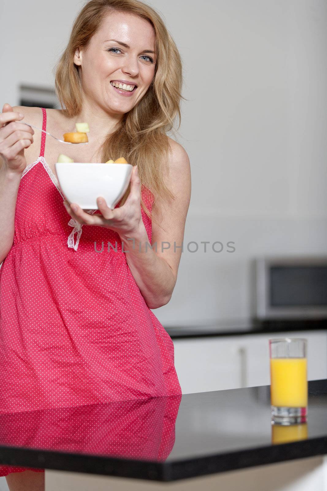 Young woman wearing pink knighty in kitchen eating breakfast