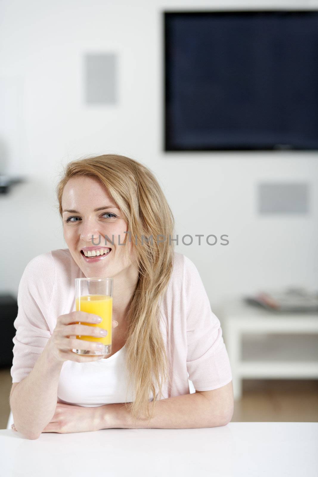 Young woman in pink shirt sitting at dining table at home with orange juice