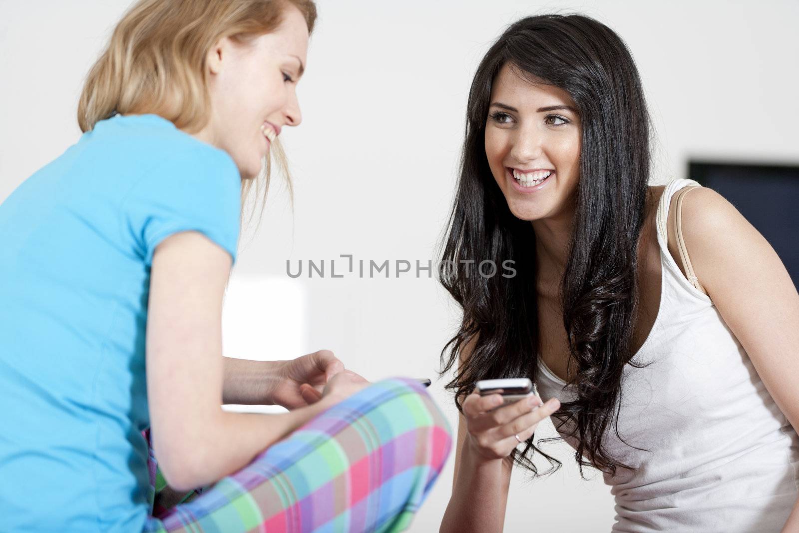 Two young woman chatting and using their mobile phones at home