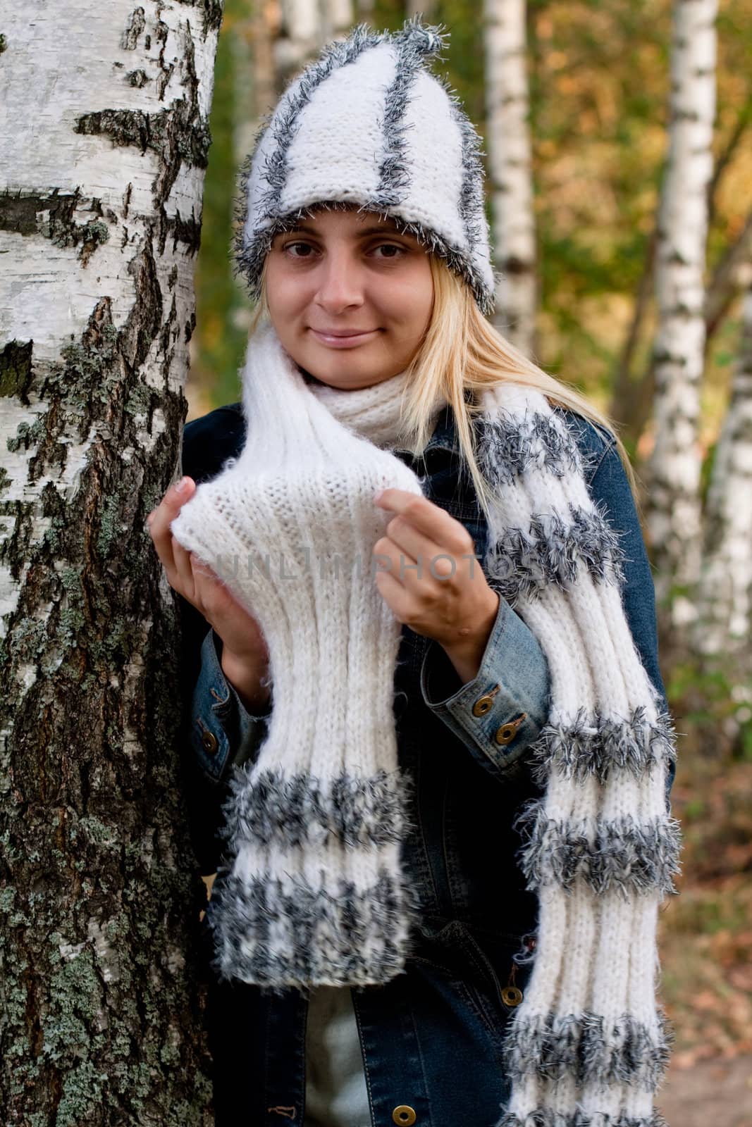 A standing girl in a cup and scarf and jeans coat in a forest
