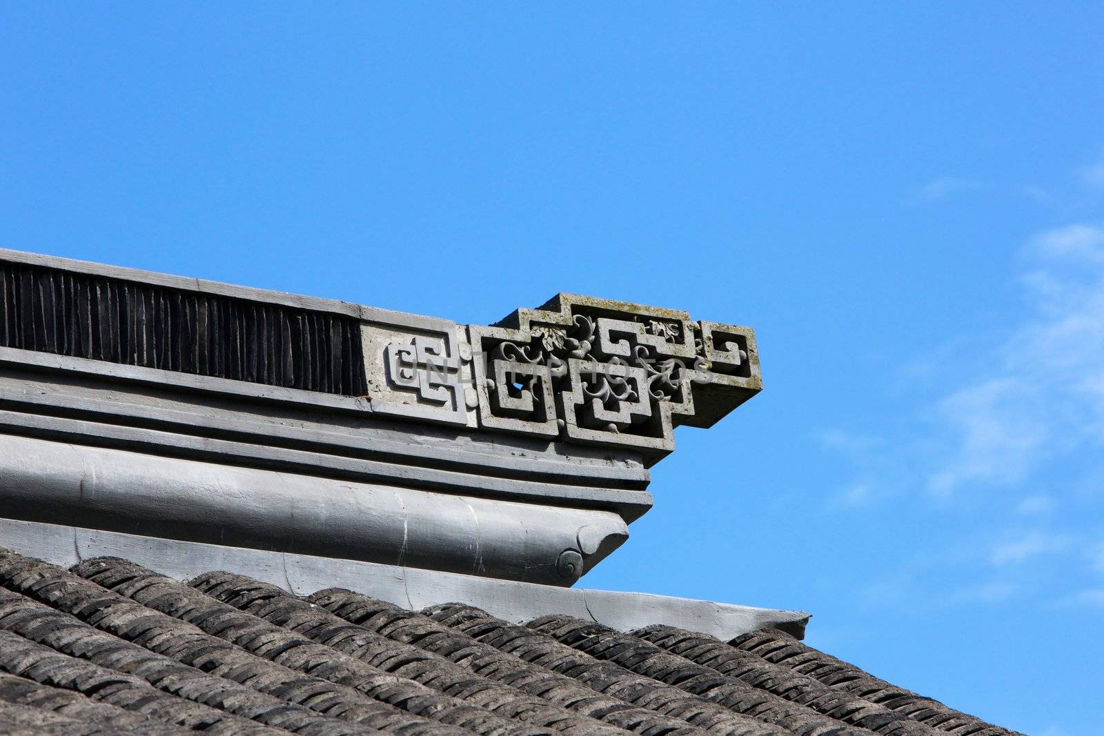 Asian design ornamentation on a chinese tile roof againt blue sky