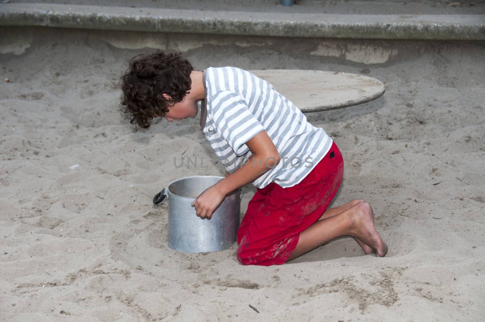 boy playing in the sandpit with sand and metal bucket