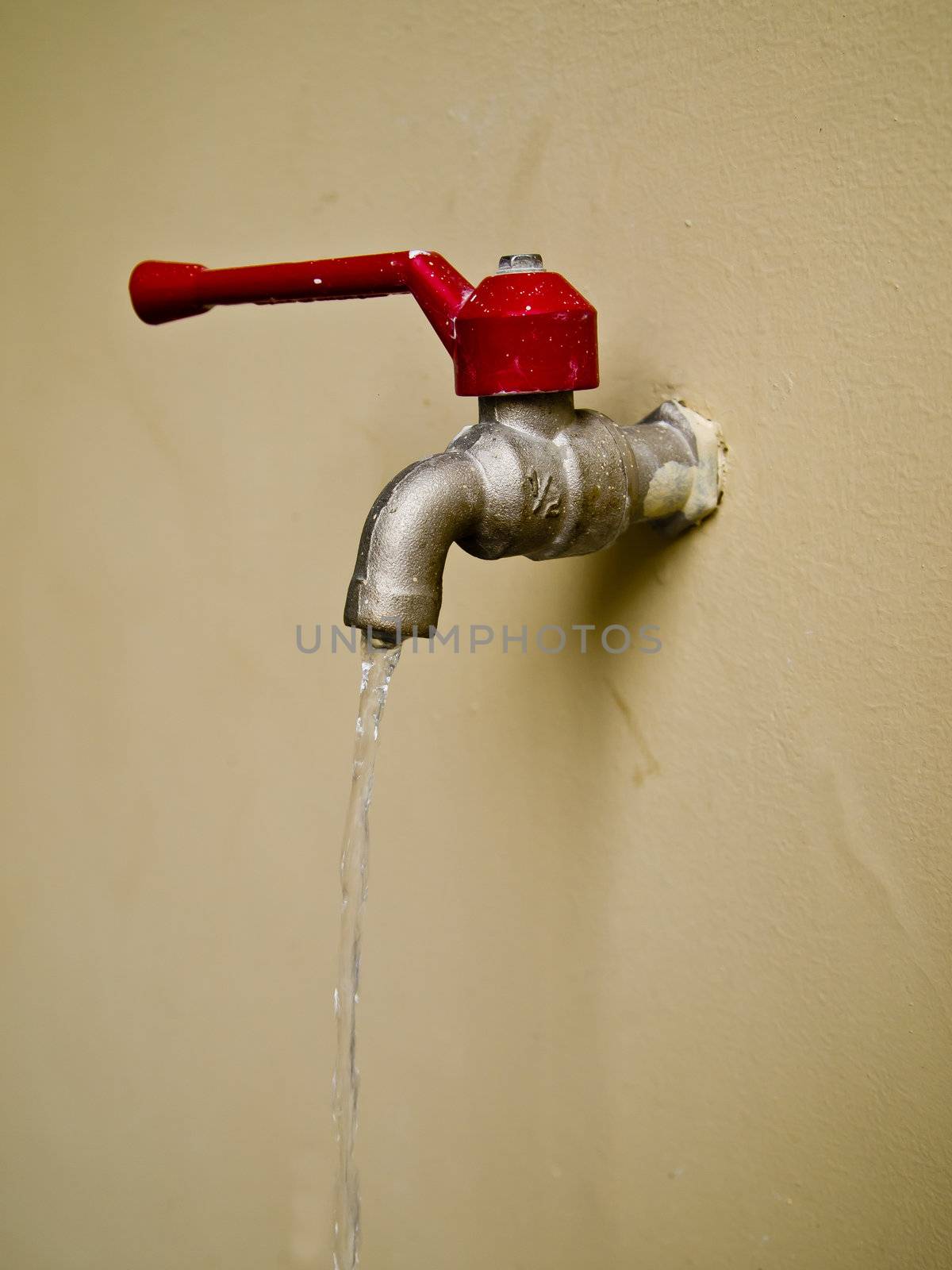 Red water tap on wall by gjeerawut