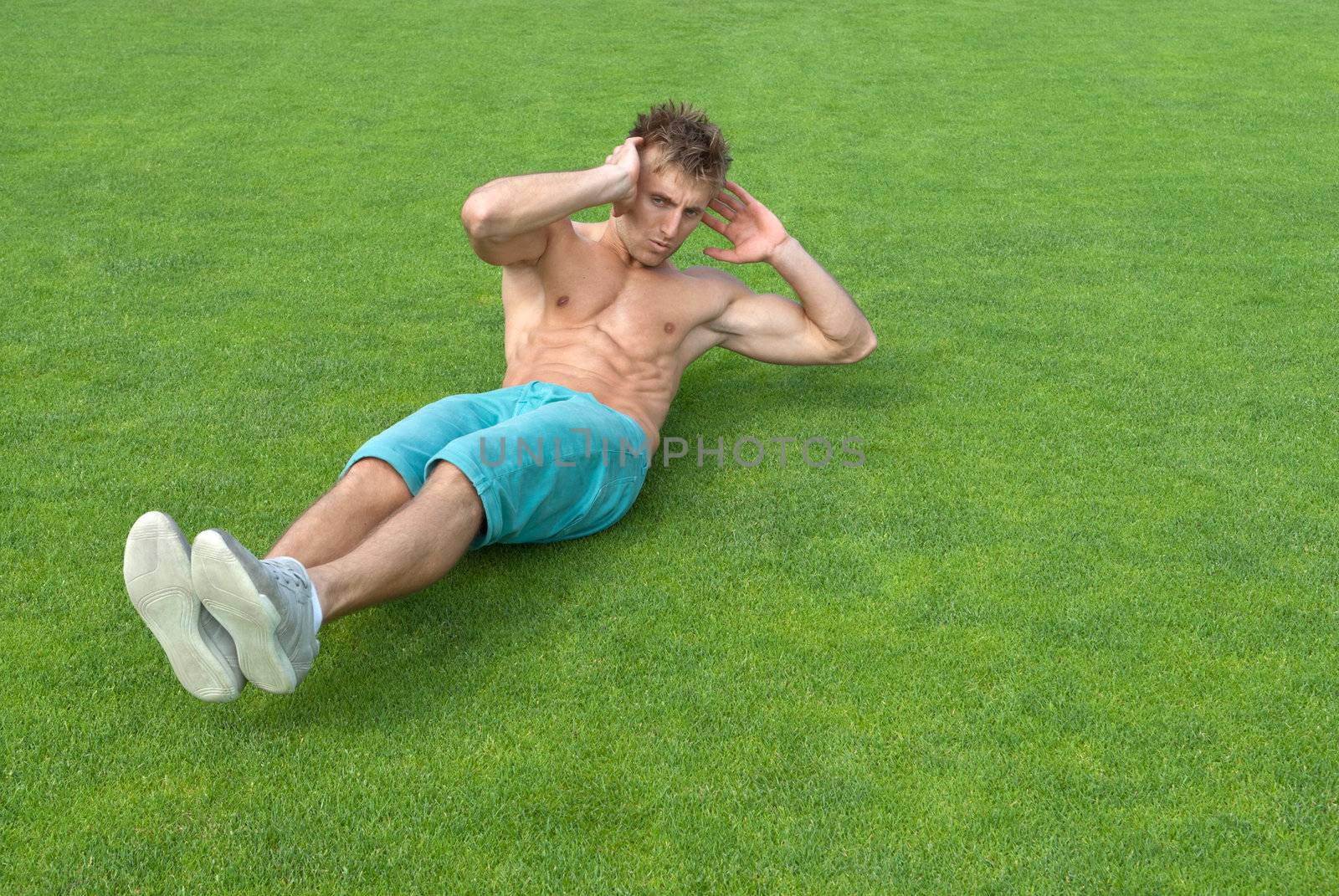 Young man doing sit-ups on green grass by anikasalsera