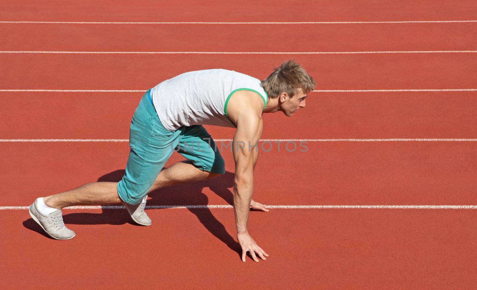 Young man on a racetrack preparing to run.