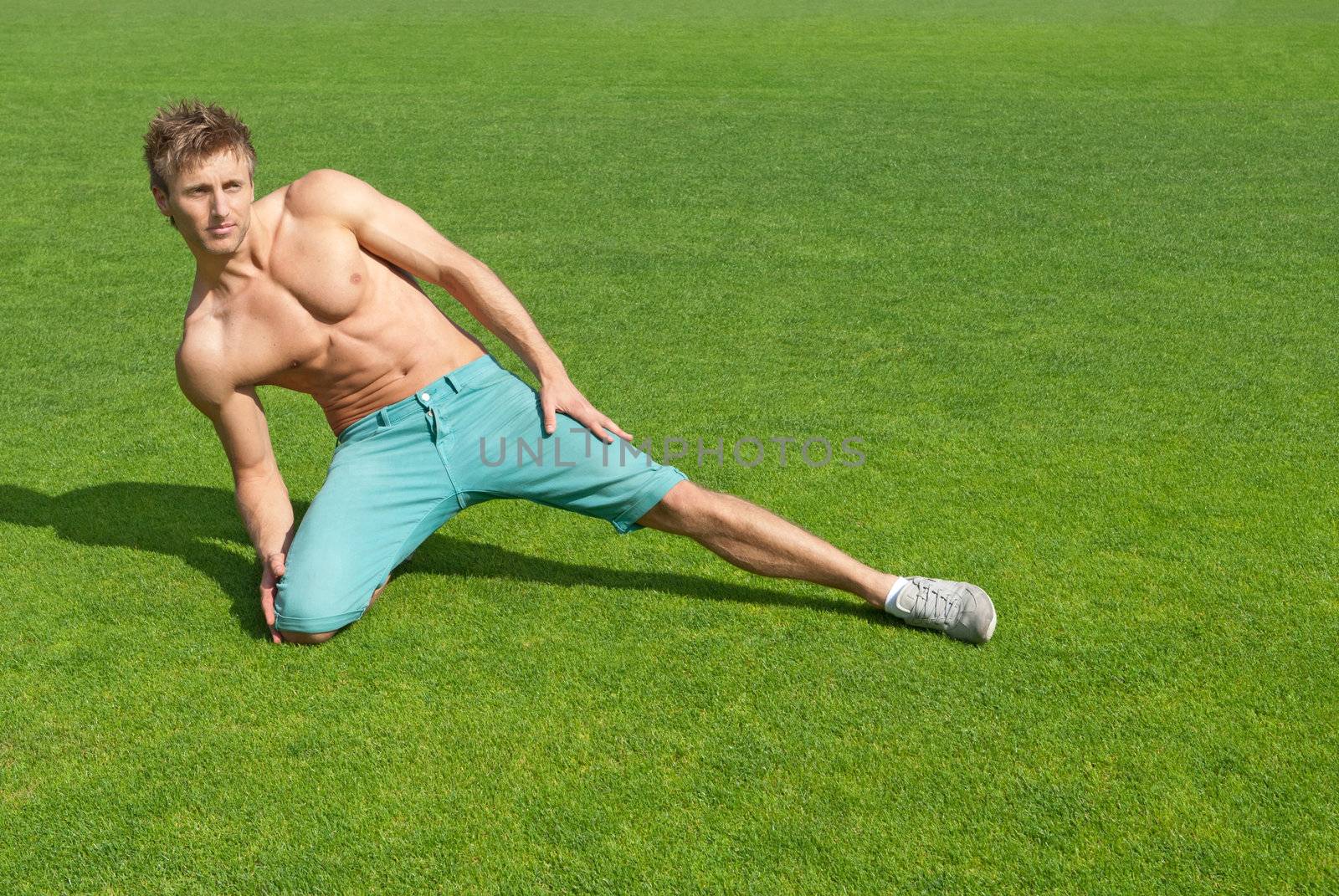 Young man training on green grass by anikasalsera