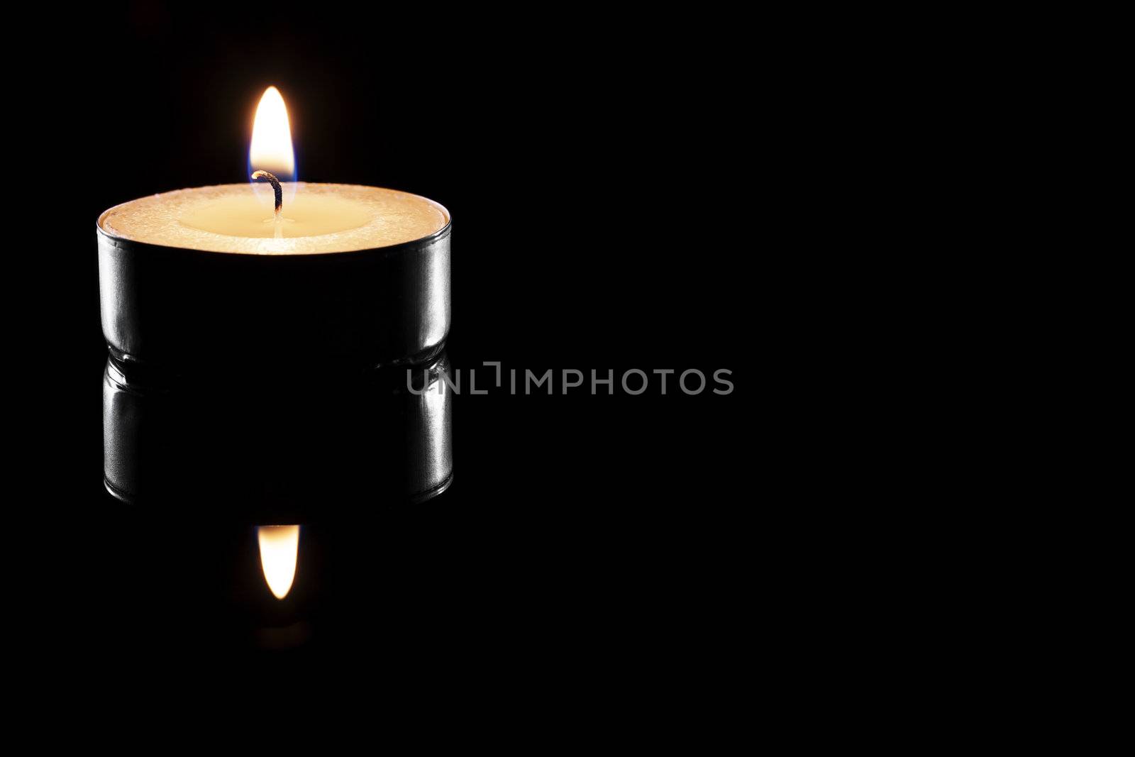 one burning tea candle on black reflective background