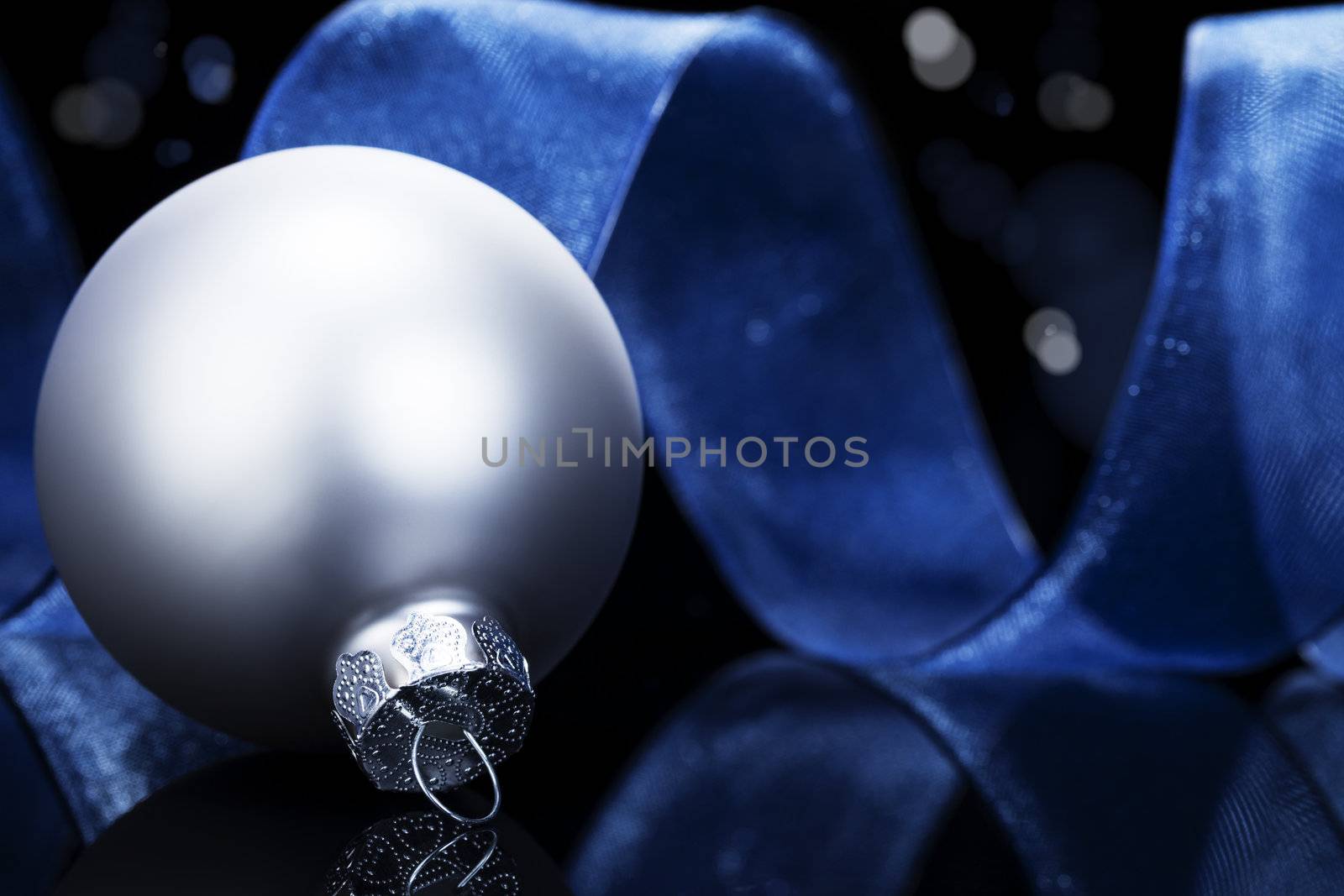 dull silver christmas ball in front of a blue ribbon on black reflective background