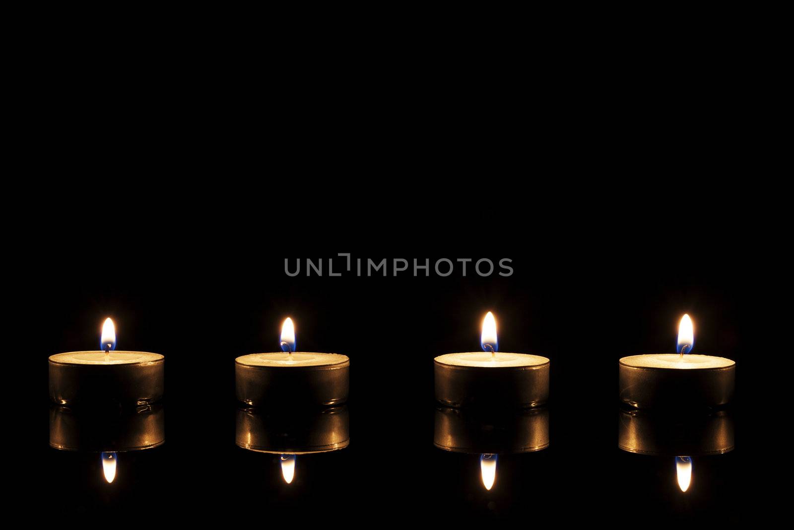 four burning tea candles on a black mirror on black background