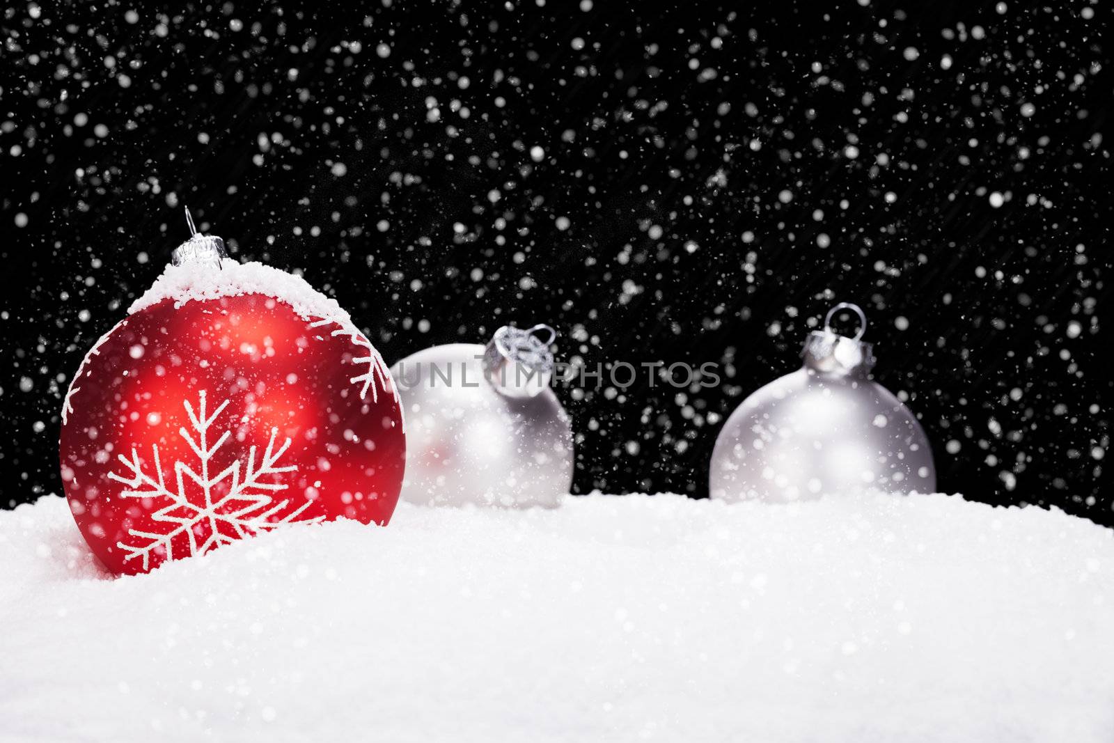 red and silver christmas balls in snow on black background while snowing