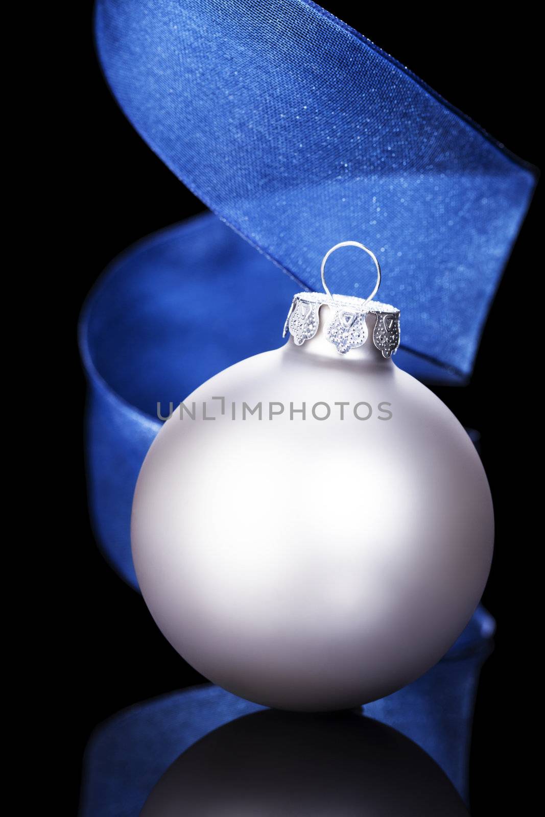 dull silver christmas ball in front of a blue ribbon on black background