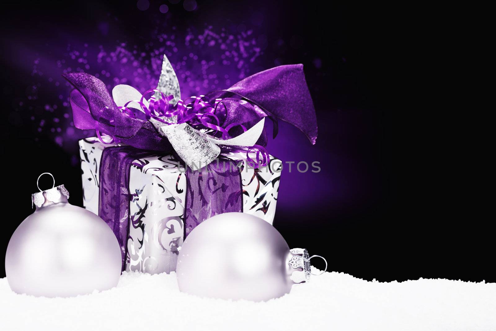 purple christmas present in snow with christmas balls and purple lightning on black background