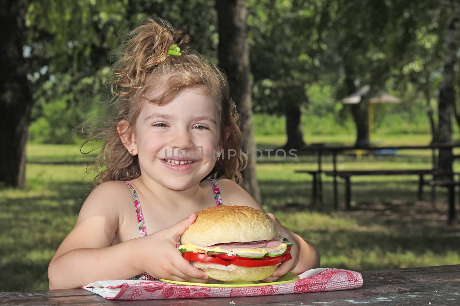 little girl with big sandwich sitting in park