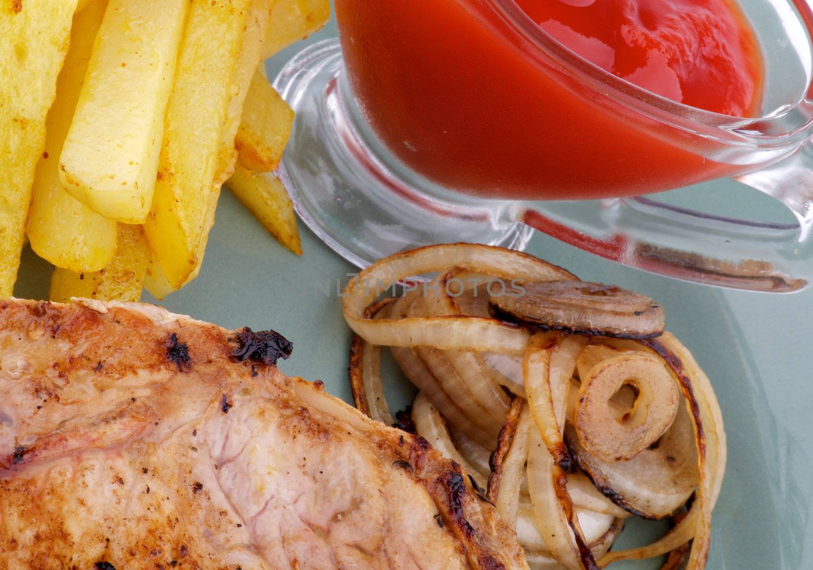 Unhealthy Lunch with Pork Steak, French Fries, Grilled Onion and Ketchup close up on green plate