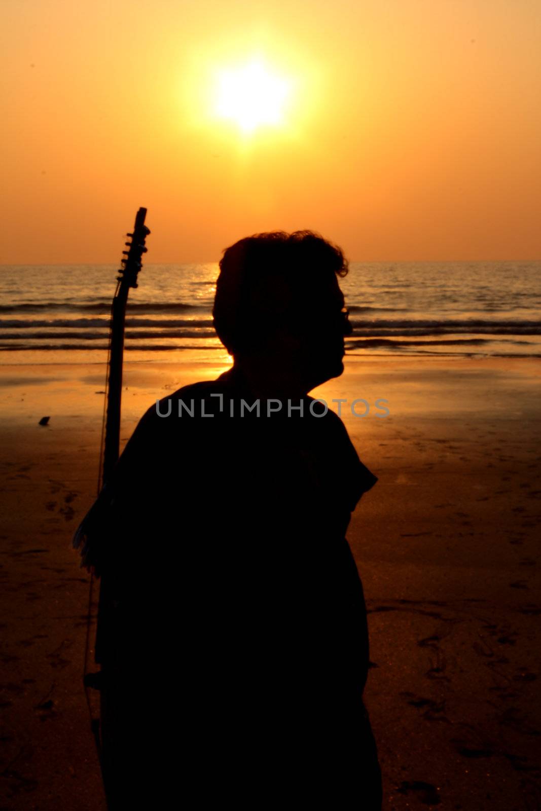 A silhouette of a lonely guitarist on a beach at sunset.
