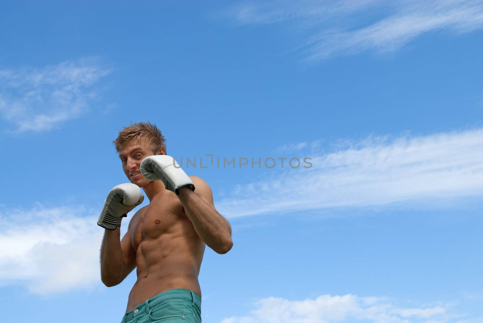 Young guy in boxing gloves, on blue sky background.