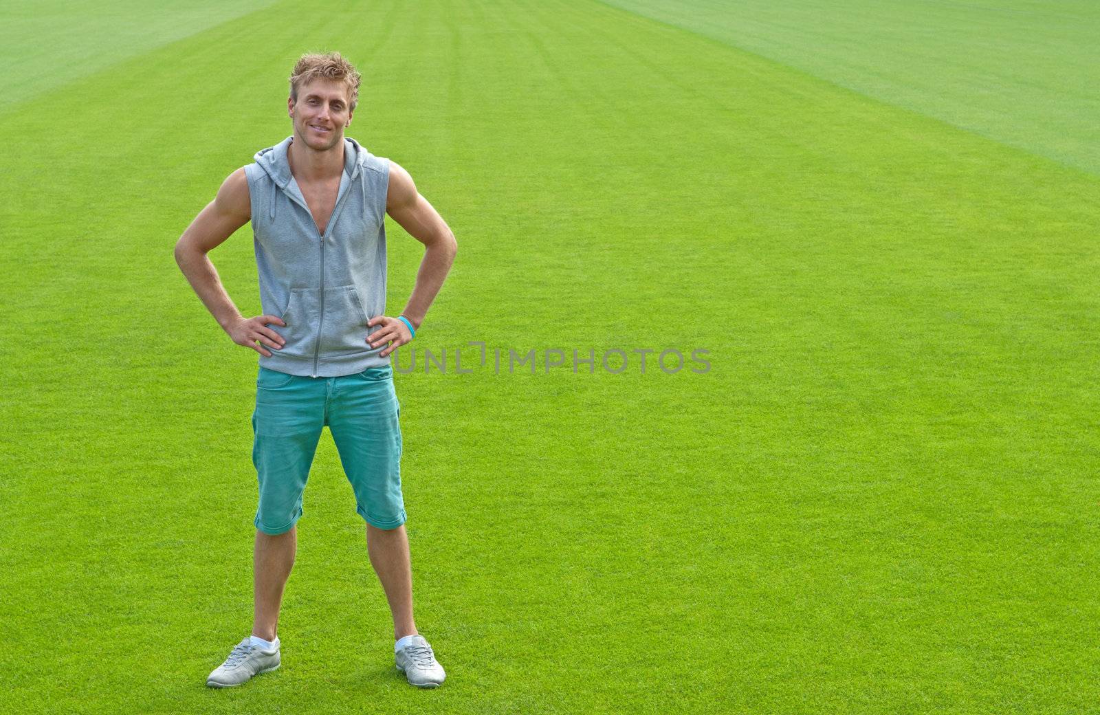 Sporty young man standing on green training field, smiling.