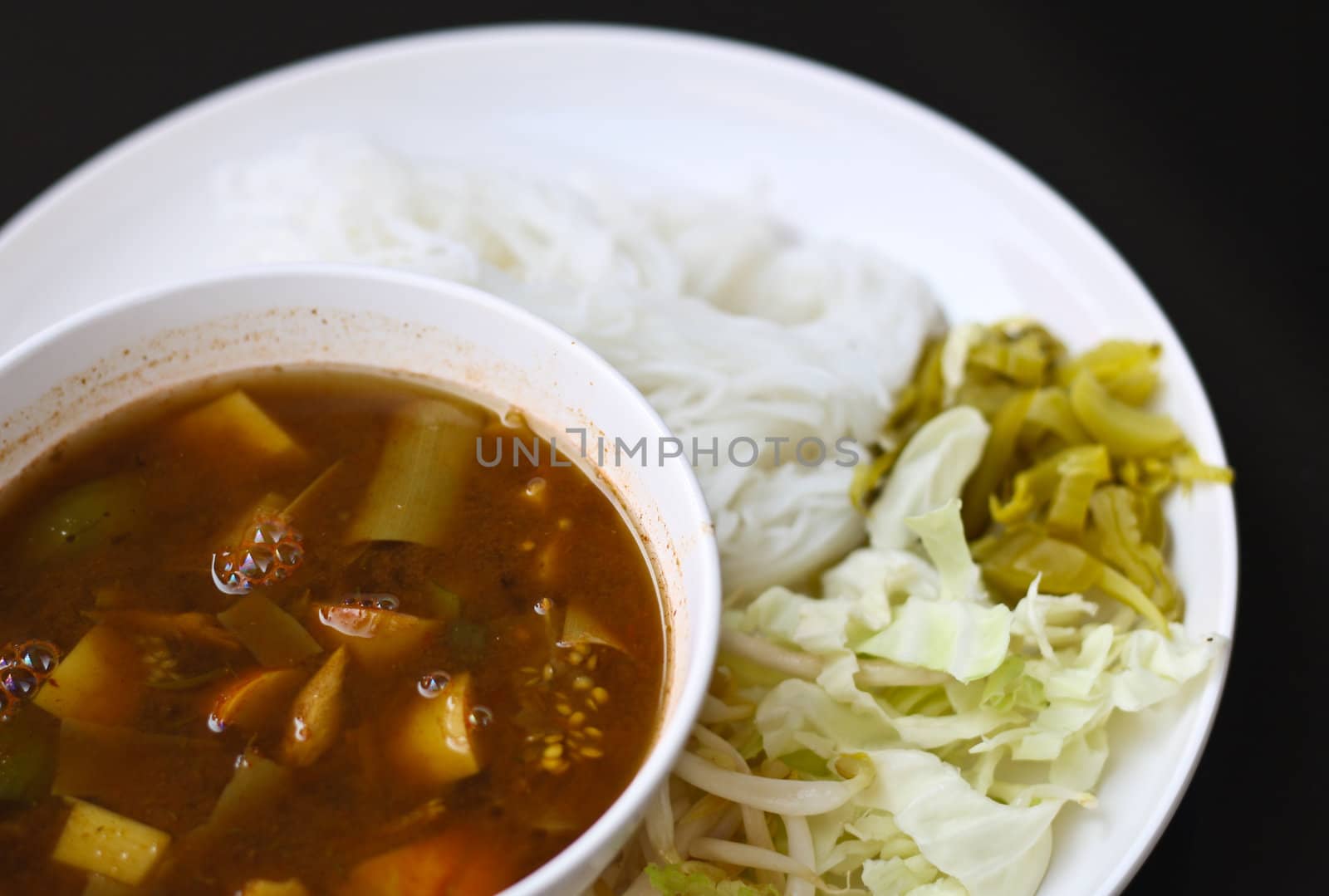 Tai curry noodles with vegetables on a white plate.