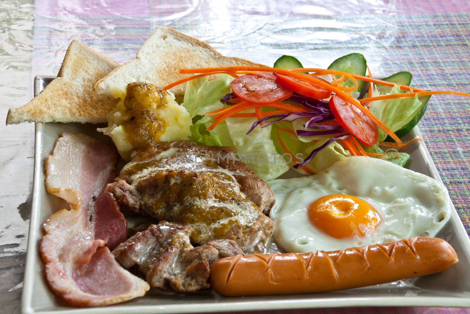 Steak pork, bacon, fried egg, sausage, bread and salad.