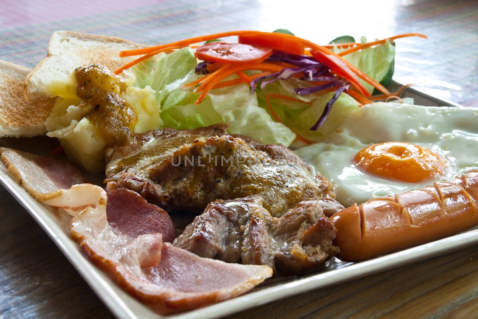 Steak pork, bacon, fried egg, sausage, bread and salad.