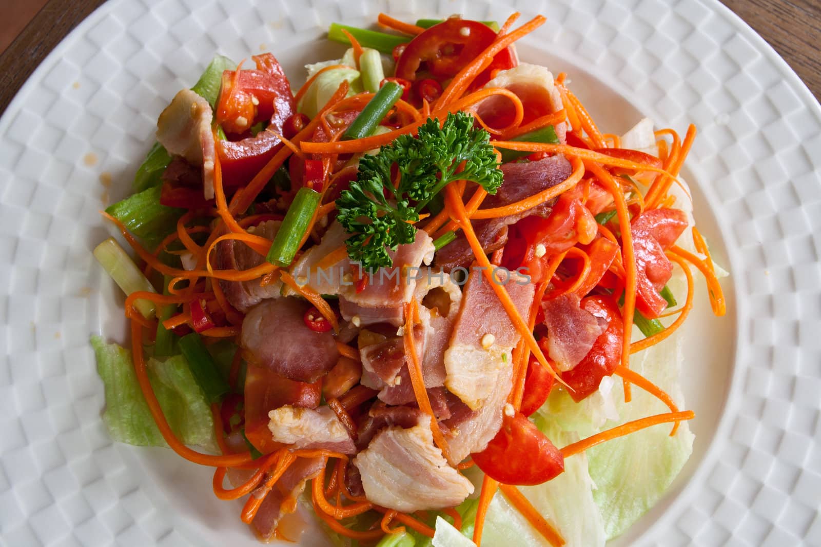 Spicy bacon salad with tomato carrot on white dish.