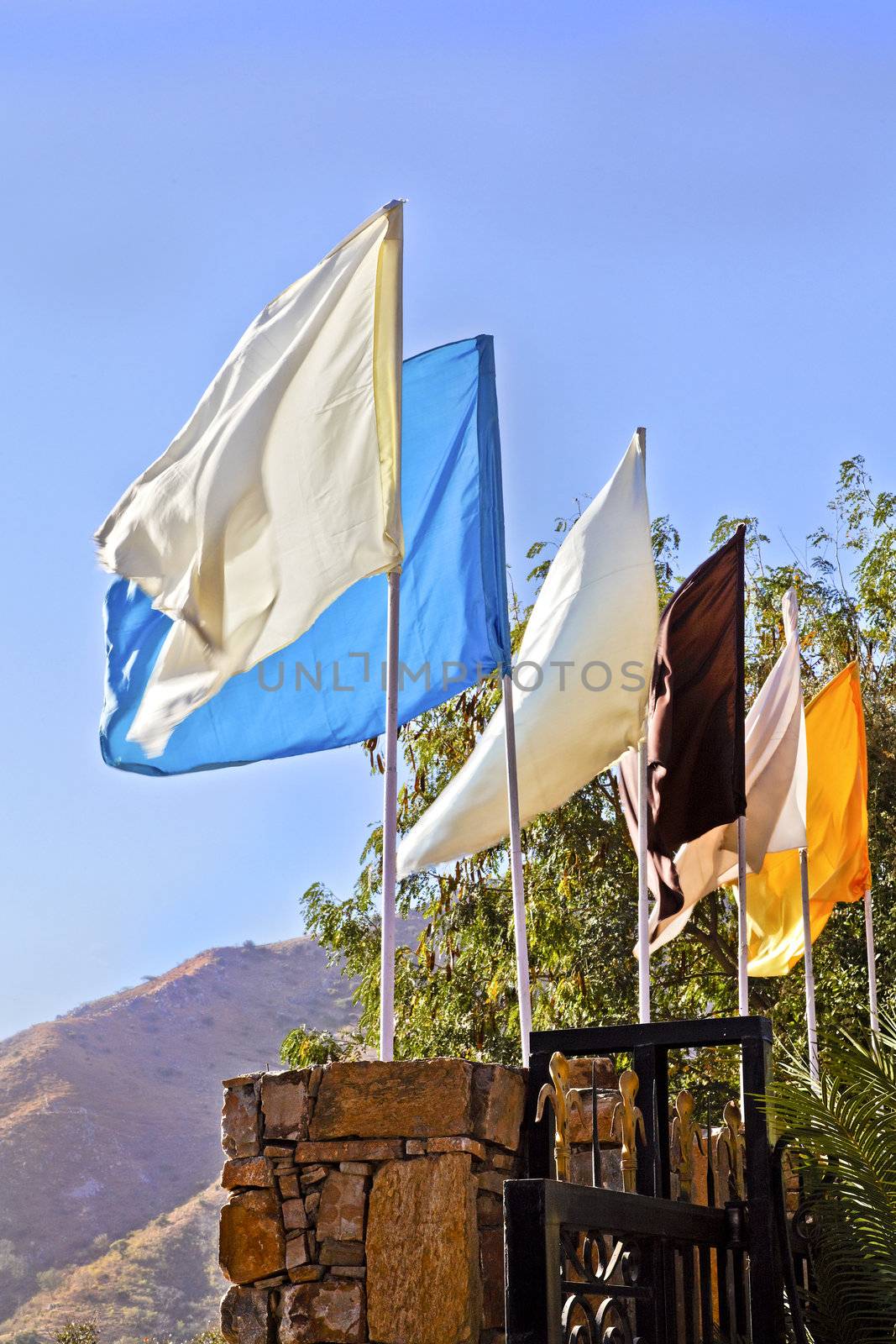 Generic portrait of a landscape incorporating plain multi coloured flags mounted on a stone wall at an entrance to a property. Location of shot was Rajasthan, India