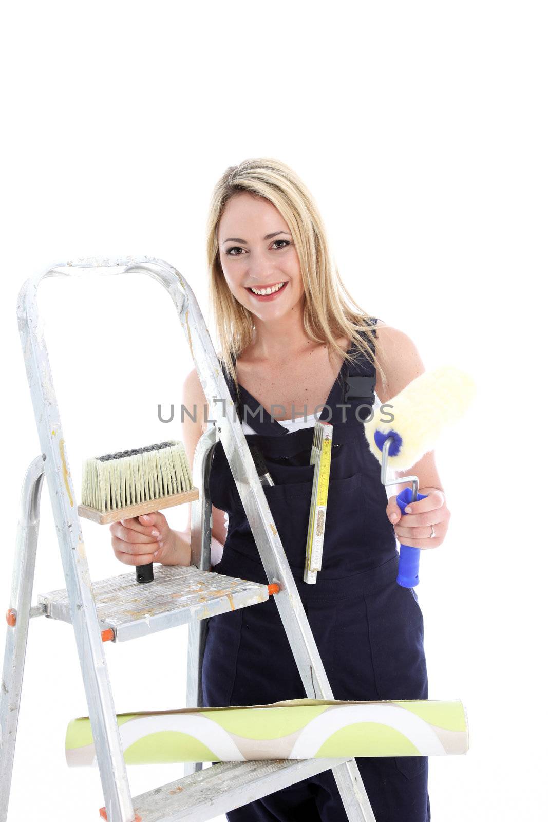 Happy housewife doing DIY standing alongside her ladder with wallpaper, roller and brush isolated on white 