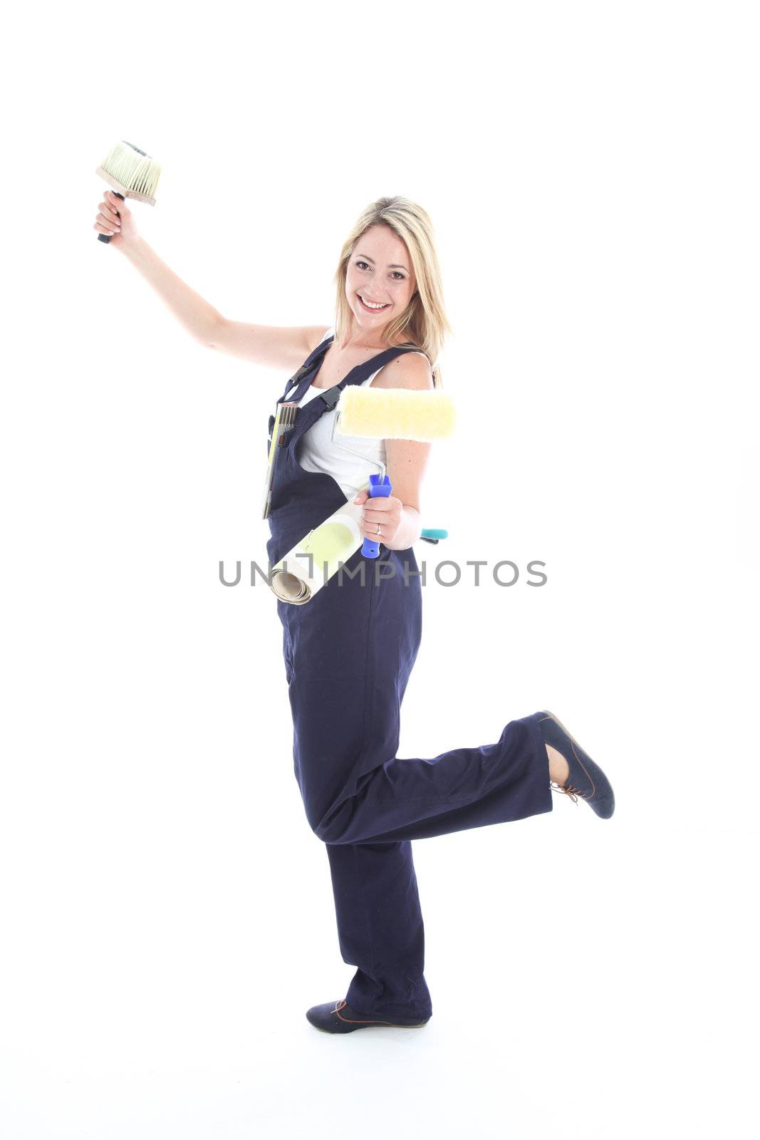 Joyful DIY woman decorator in dungarees posing playfully on one foot with a roll of wallpaper and brushes Joyful DIY woman decorator in dungarees posingplayfully on one foot with a roll of wallpaper and brushes 