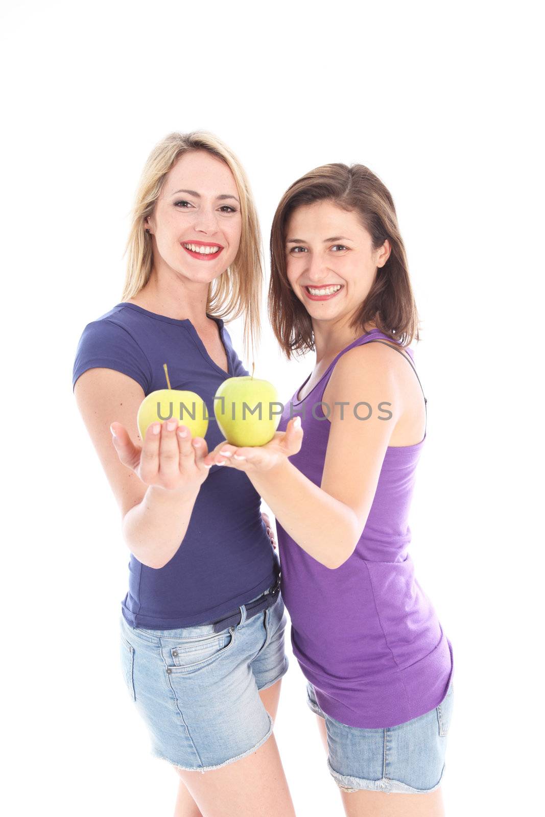 Two happy young women with apples balanced on their open palms standing facing each other in casual denim shorts 