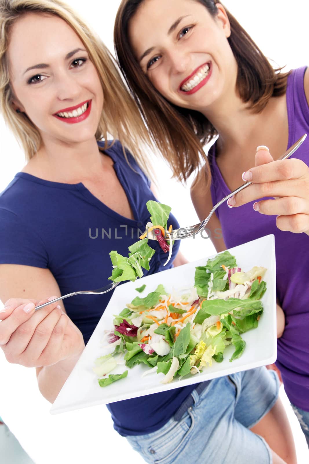 Two attractive happy casual young health conscious friends enjoying a green salad eating off a shared plate Two attractive happy casual young health conscious friends enjoying a green salad eating off a shared plate 