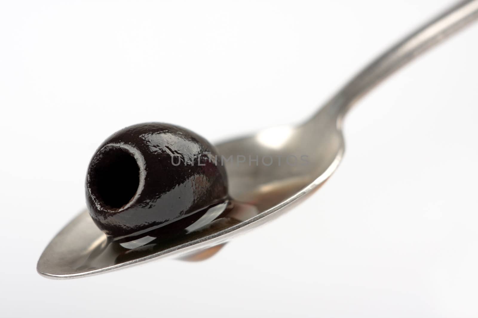 Black olive on spoon against white background