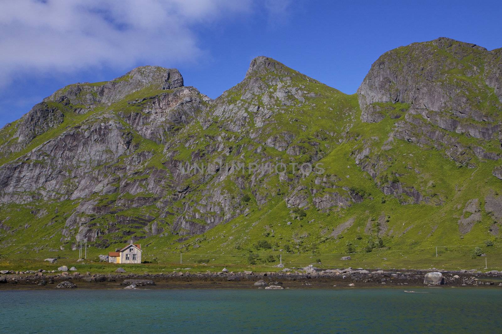 Old abandoned house by fjord surrounded by tall mountain peaks on Lofoten islands, Norway