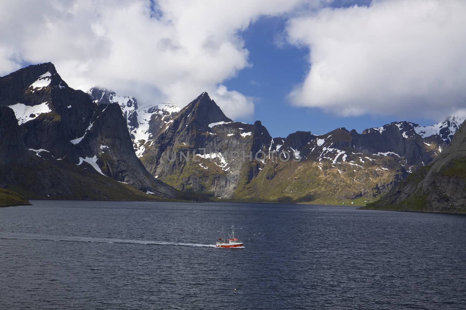 Small fishing boat passing through a scenic fjord on Lofoten islands, Norway