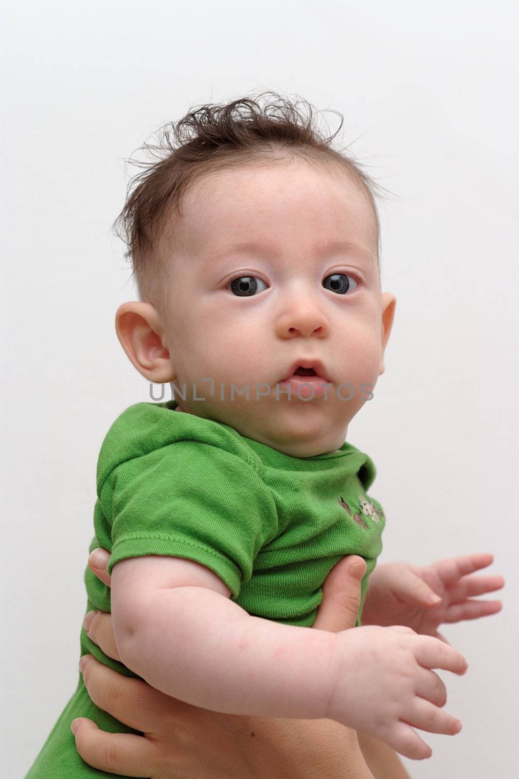 Cute serious baby held by his mother turns toward the camera