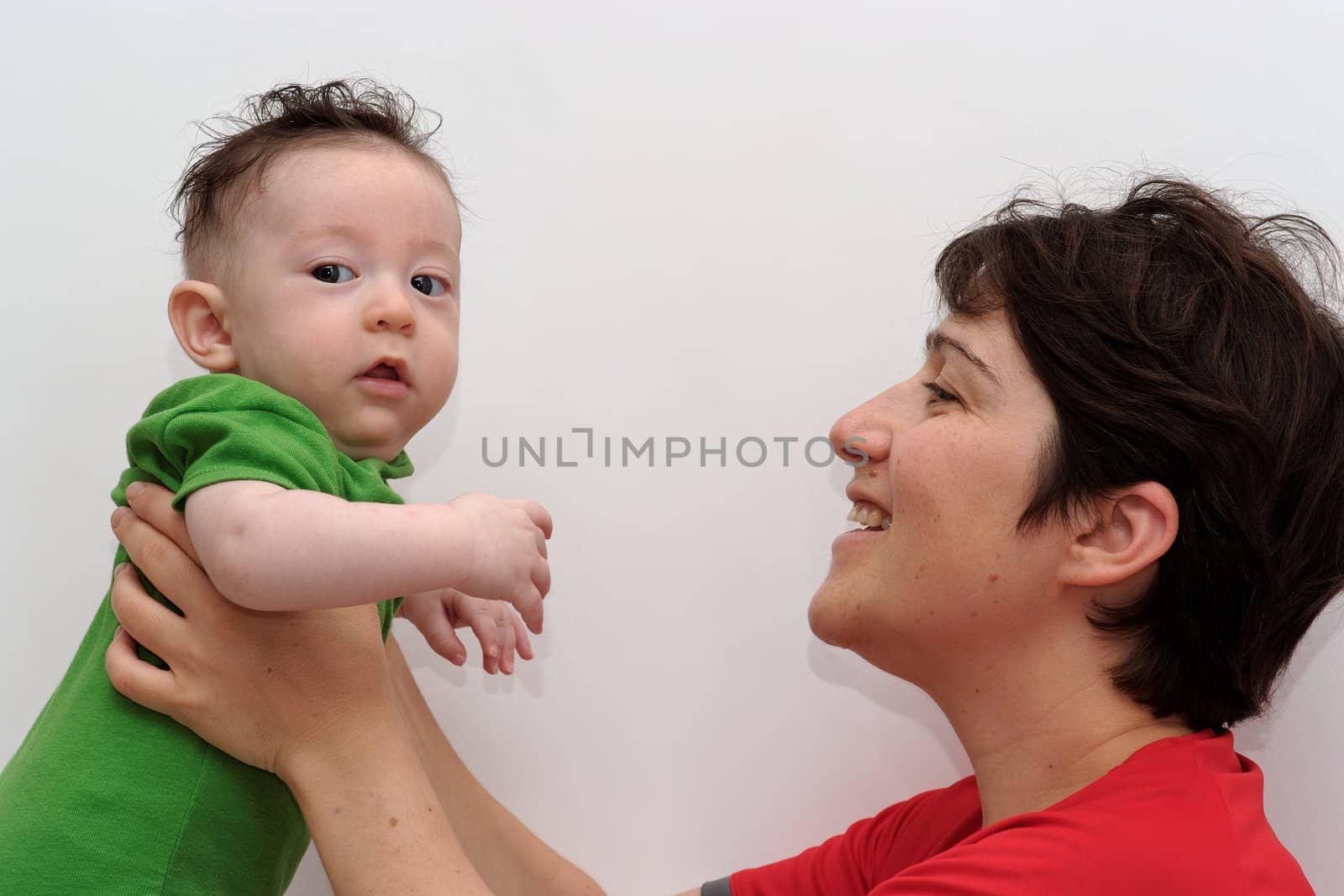 Cute baby held by his smiling mother looks toward the camera