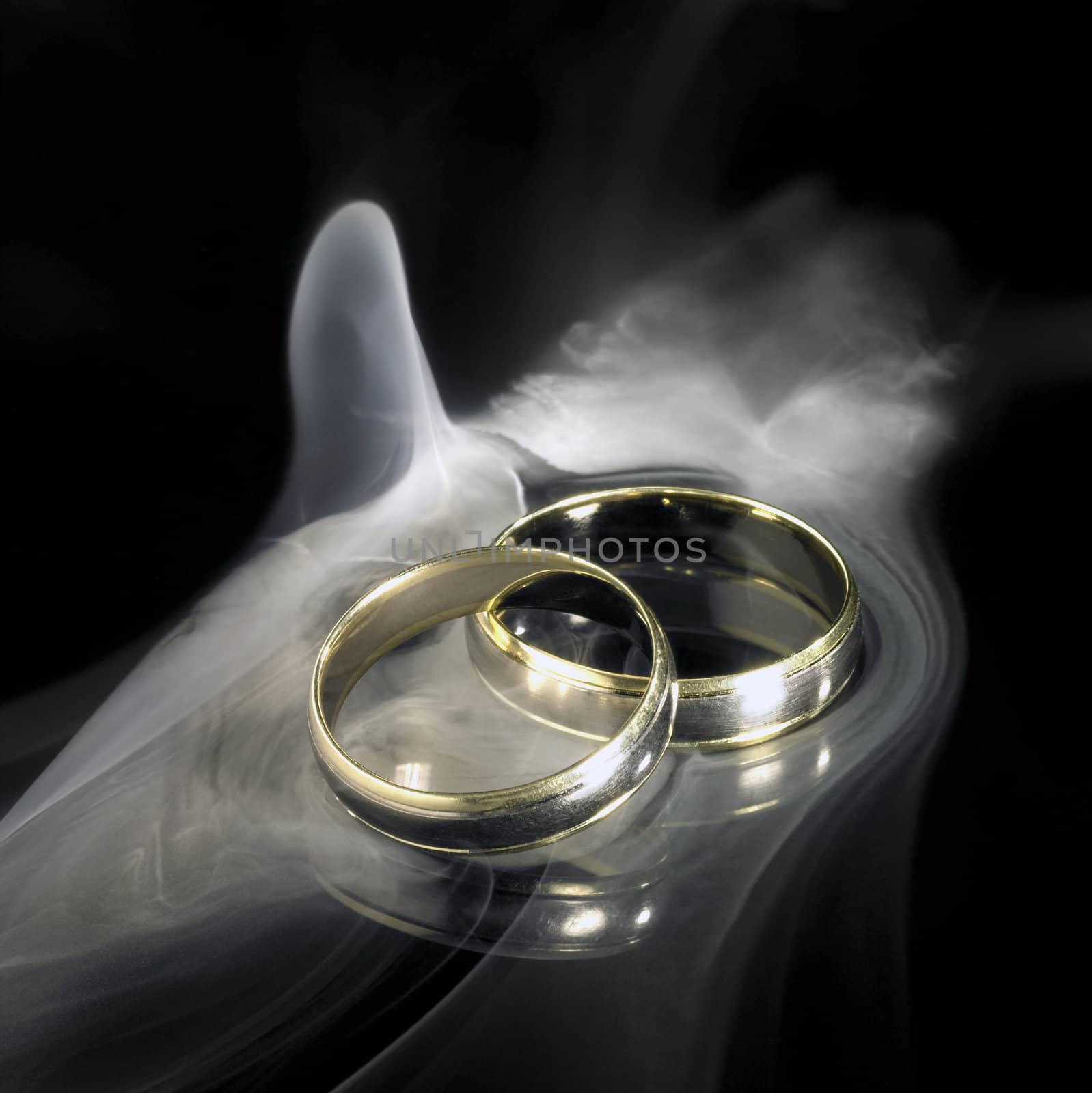 studio photography of two golden wedding rings and smoke in black reflective back