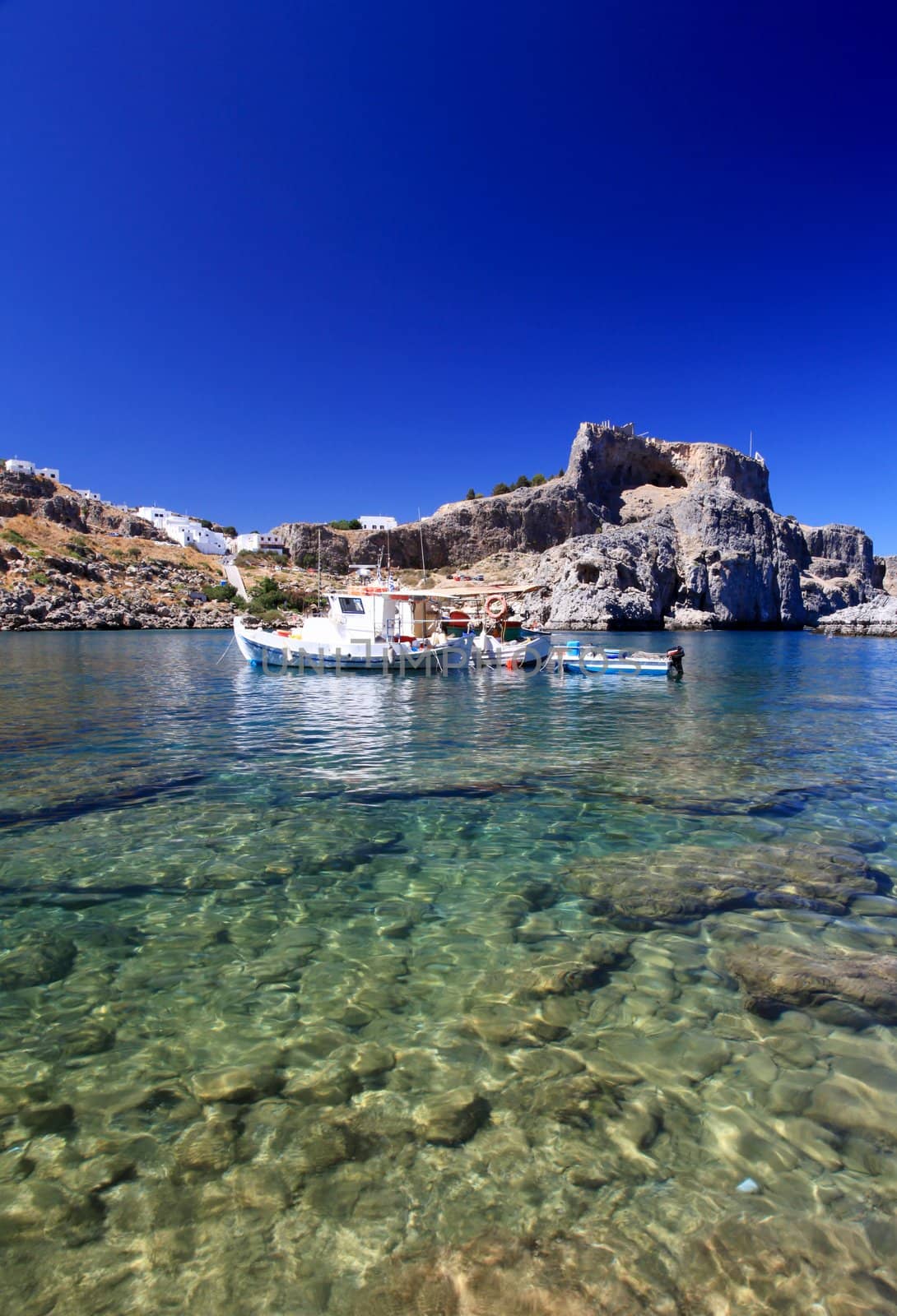 Emerald water at beautiful St Pauls Bay shadowed by the temple and castle ruins at Lindos 