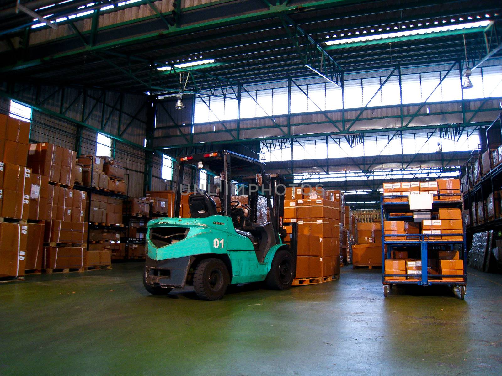 Green forklift in warehouse by gjeerawut