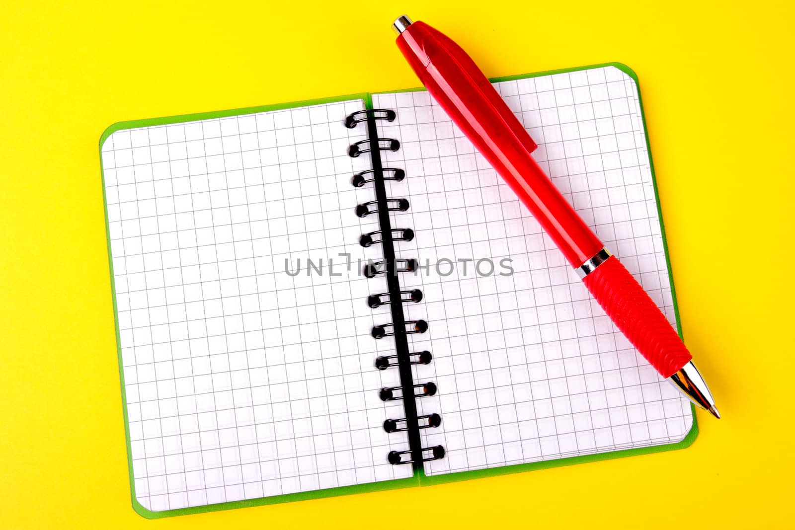 Opened notebook squared pagewith red pen over it on yellow background 