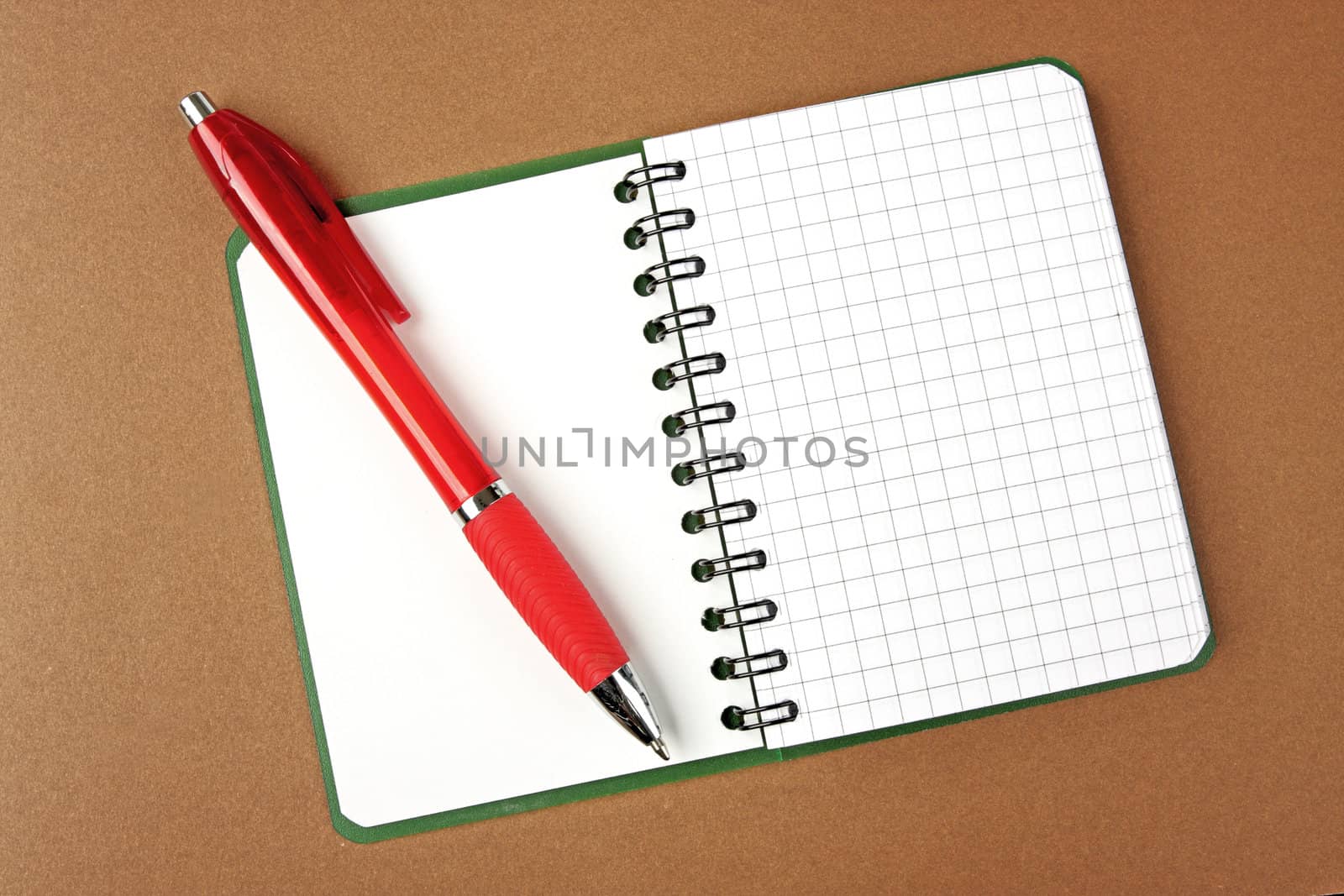 Opened notebook squared pagewith red pen over it on brown backgr by Verdateo