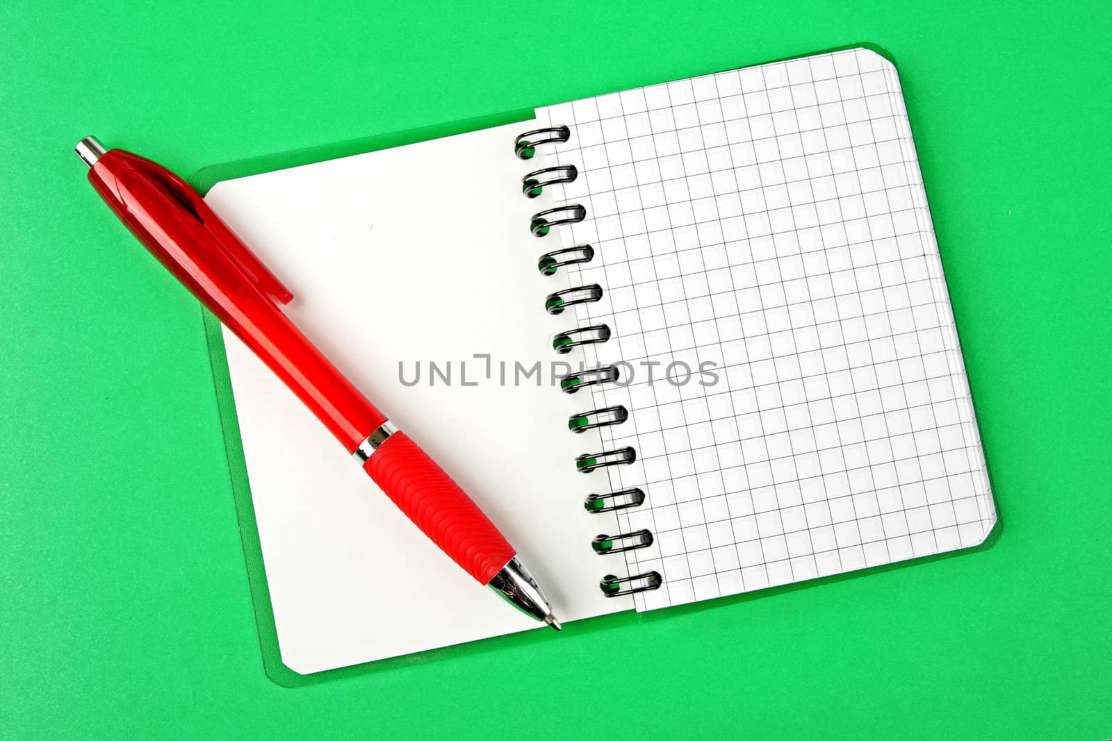 Opened notebook squared pagewith red pen over it on green background 