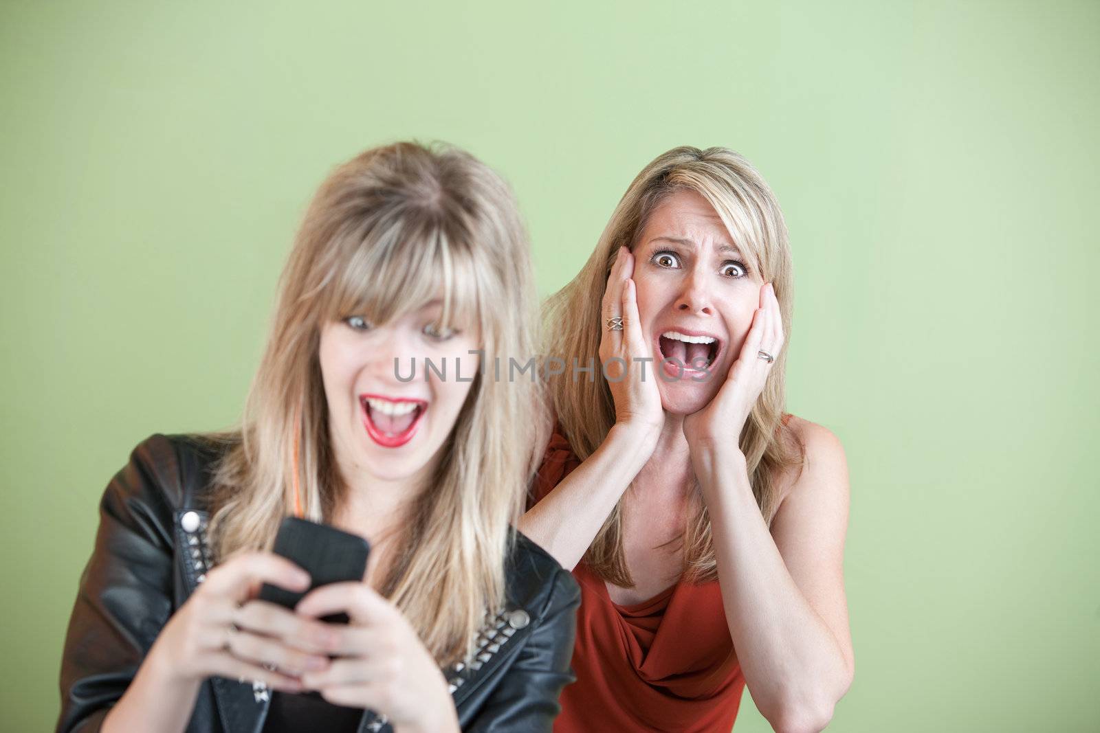 Excited daughter texting with shocked mom behind her over green background