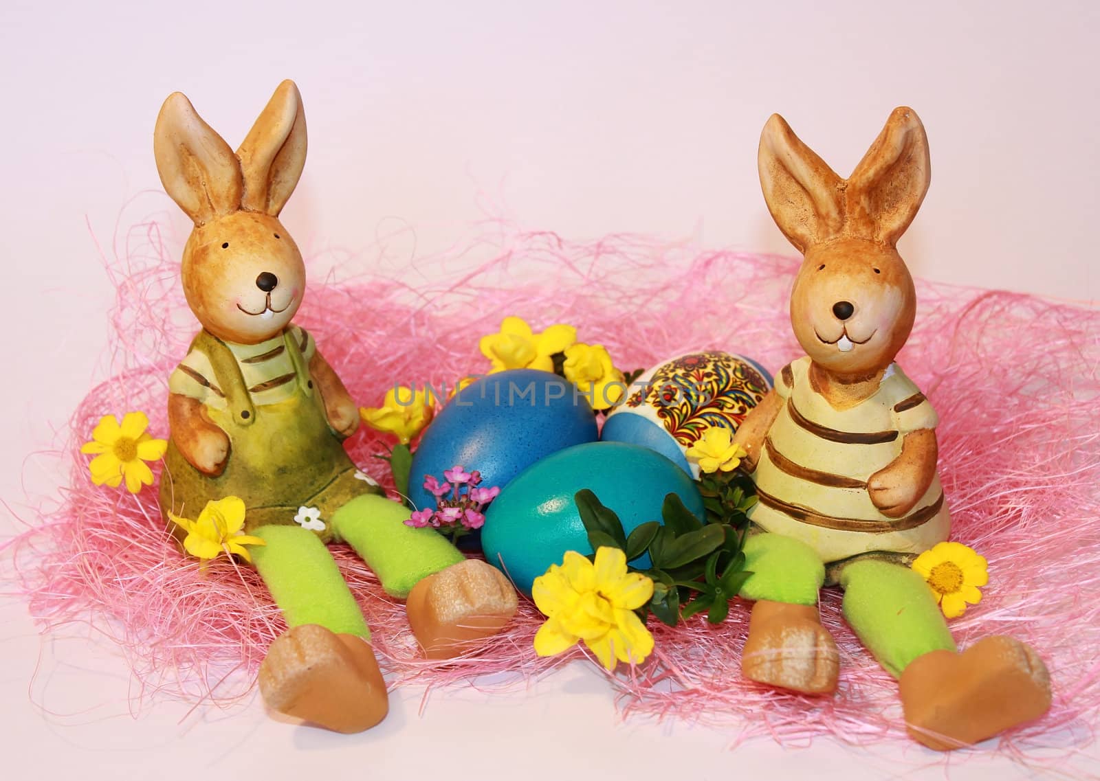 toy rabbits are sitting near the dyed Easter eggs on a pink background